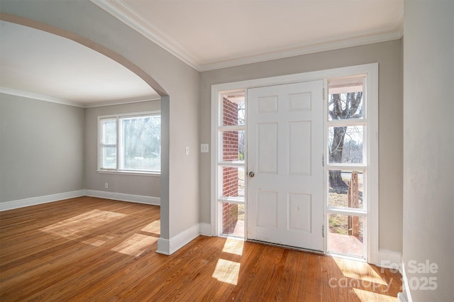 foyer entrance featuring baseboards, light wood-style flooring, arched walkways, and crown molding