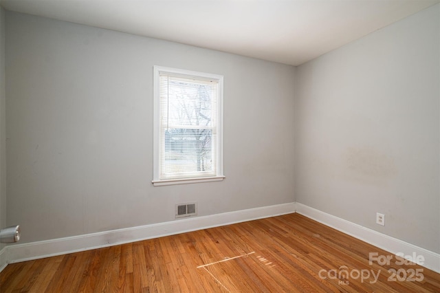 spare room with wood finished floors, visible vents, and baseboards