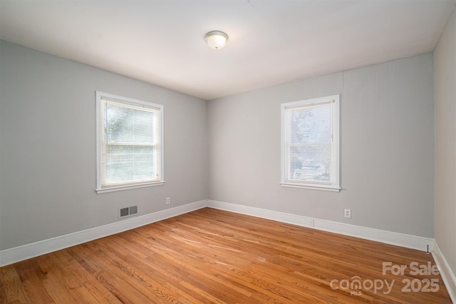 empty room featuring light wood finished floors, plenty of natural light, visible vents, and baseboards