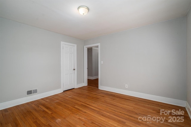 empty room featuring wood finished floors, visible vents, and baseboards