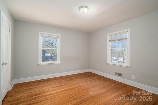 empty room featuring baseboards, visible vents, plenty of natural light, and light wood finished floors