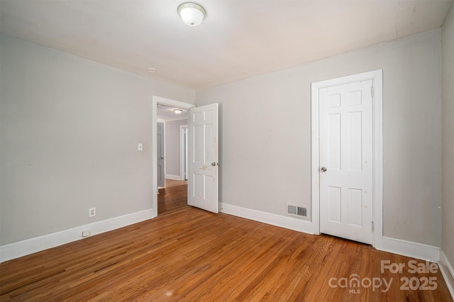 spare room featuring wood finished floors, visible vents, and baseboards