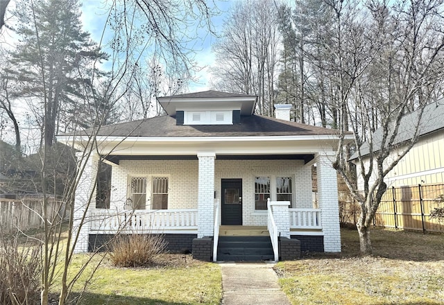 bungalow-style house featuring a porch, fence, and brick siding