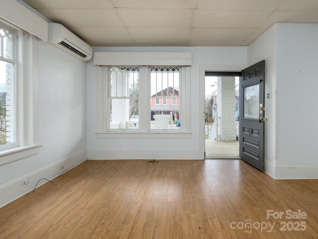 unfurnished room with a wealth of natural light, a wall mounted air conditioner, baseboards, and wood finished floors