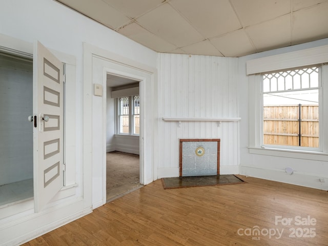 unfurnished living room with a paneled ceiling, baseboards, and wood finished floors