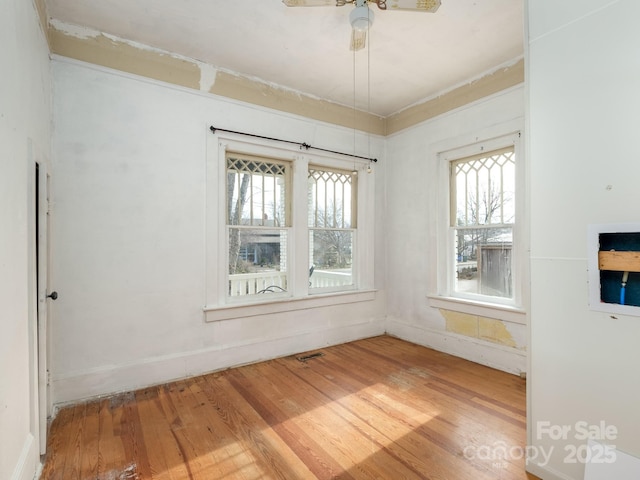 spare room with a ceiling fan, baseboards, a wealth of natural light, and wood finished floors