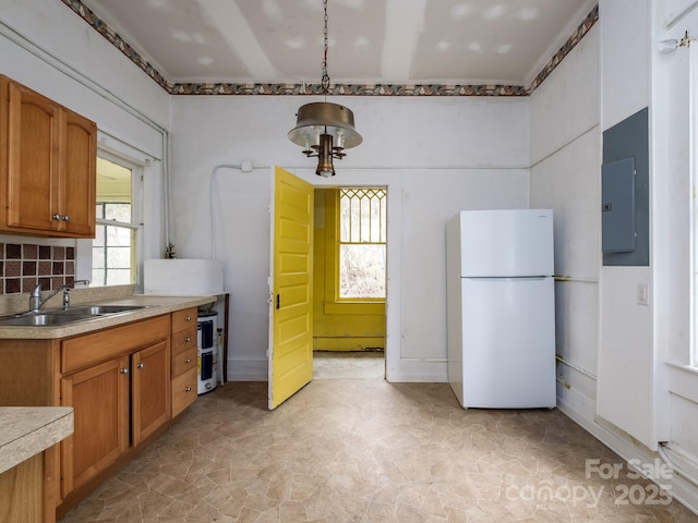 kitchen with brown cabinetry, freestanding refrigerator, light countertops, and a sink