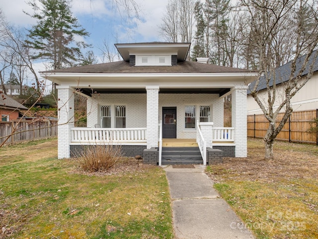 bungalow-style home featuring covered porch, brick siding, a front lawn, and fence