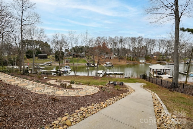 view of property's community with a dock, a water view, fence, and boat lift