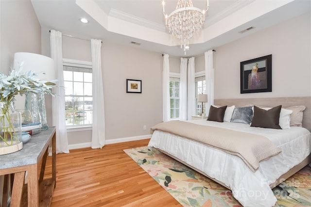 bedroom with multiple windows, a raised ceiling, visible vents, and light wood-style floors