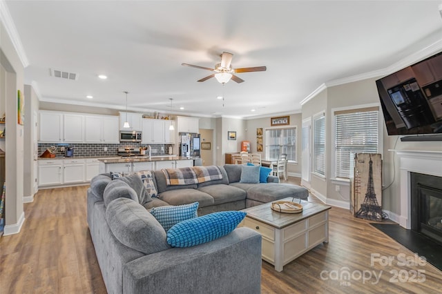 living room with ornamental molding, wood finished floors, a glass covered fireplace, and visible vents