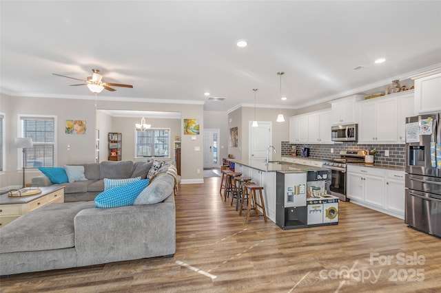 kitchen with open floor plan, stainless steel appliances, a center island with sink, and white cabinets