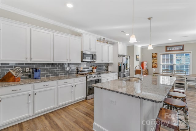 kitchen featuring appliances with stainless steel finishes, pendant lighting, white cabinetry, and an island with sink