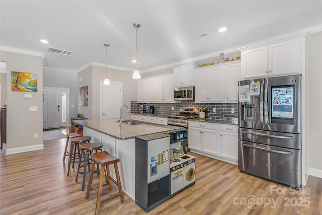 kitchen with dark stone counters, an island with sink, stainless steel appliances, white cabinetry, and a sink