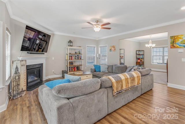 living room featuring baseboards, a fireplace with flush hearth, wood finished floors, crown molding, and ceiling fan with notable chandelier