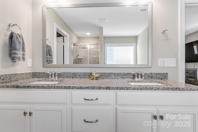 full bathroom with double vanity, a shower stall, visible vents, and a sink