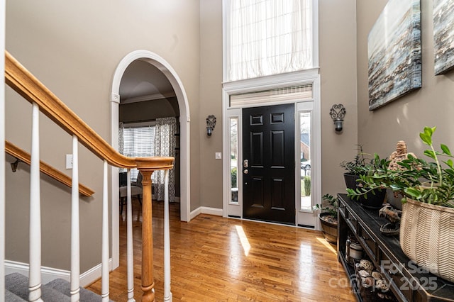 entryway with baseboards, arched walkways, a towering ceiling, stairs, and light wood-style floors