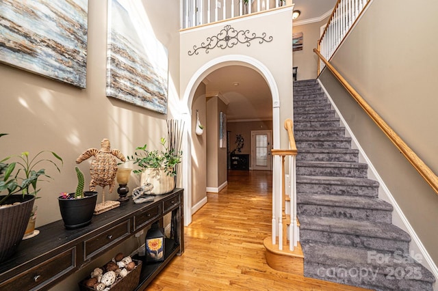 entryway featuring arched walkways, a high ceiling, stairs, ornamental molding, and light wood-type flooring