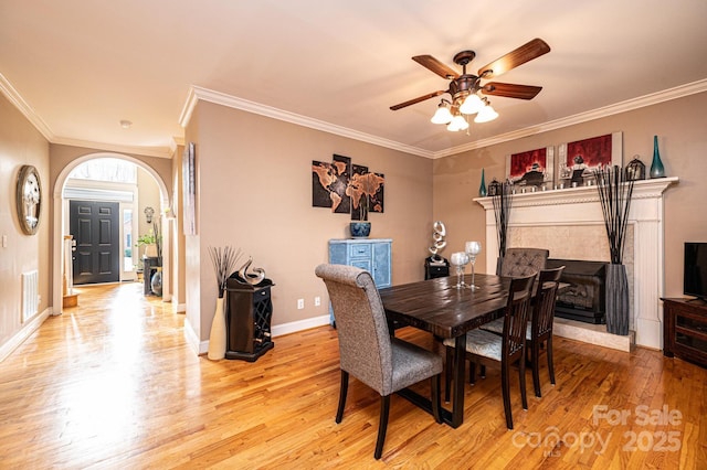 dining area featuring light wood finished floors, baseboards, visible vents, arched walkways, and ornamental molding