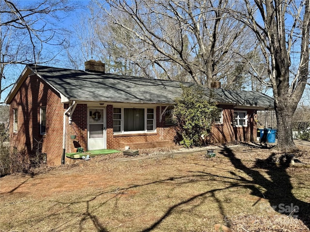 view of front facade featuring brick siding, a chimney, a front lawn, and roof with shingles