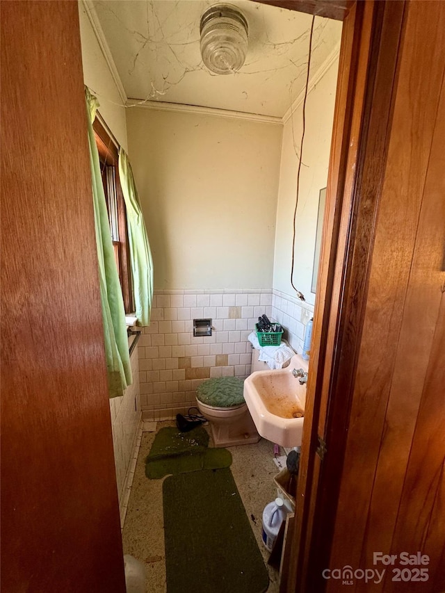 half bath featuring toilet, a wainscoted wall, a sink, tile walls, and ornamental molding