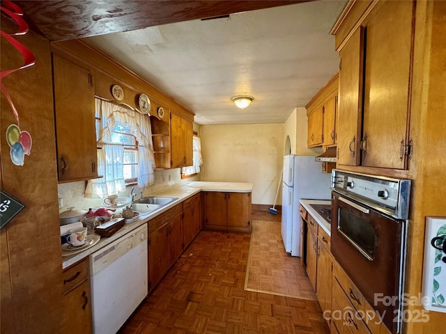 kitchen featuring white appliances, brown cabinetry, light countertops, under cabinet range hood, and a sink