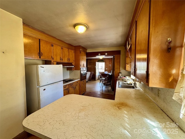 kitchen with brown cabinets, freestanding refrigerator, a peninsula, light countertops, and a sink