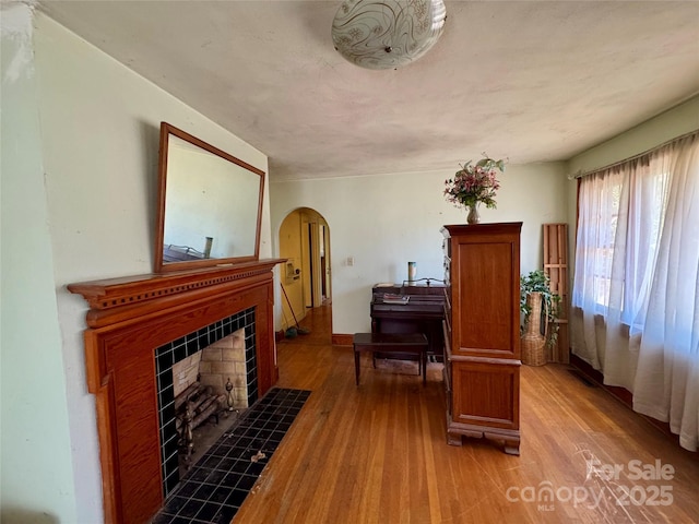 living area with light wood finished floors, arched walkways, and a tiled fireplace