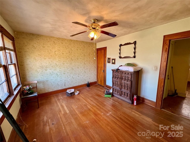 unfurnished living room with ceiling fan, baseboards, and wood finished floors