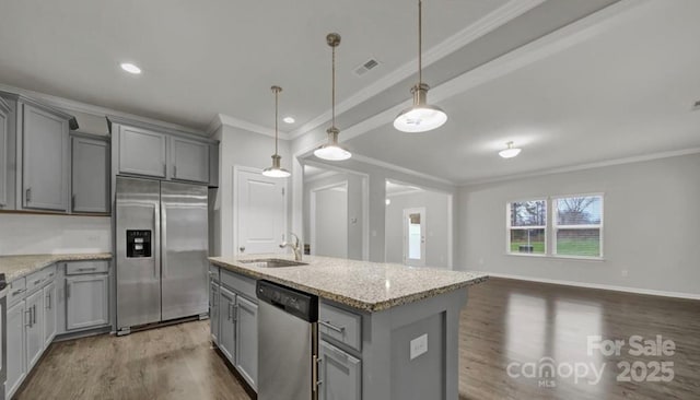 kitchen featuring stainless steel appliances, a sink, gray cabinets, an island with sink, and decorative light fixtures