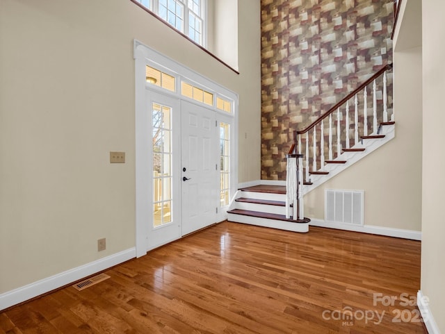 foyer featuring wood-type flooring, visible vents, a towering ceiling, and baseboards