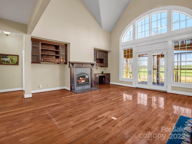 unfurnished living room with a wealth of natural light, french doors, wood finished floors, and a tile fireplace