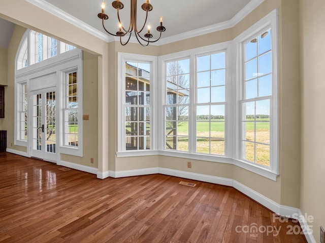 unfurnished dining area with crown molding, a notable chandelier, baseboards, and wood finished floors