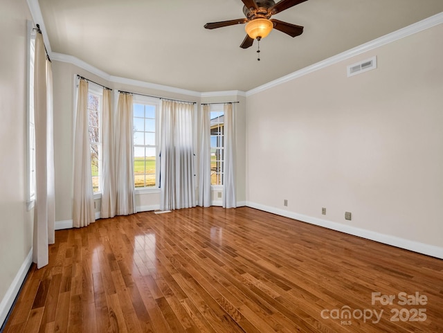 spare room with baseboards, visible vents, ceiling fan, wood finished floors, and crown molding