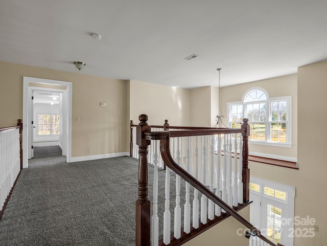 corridor with baseboards, visible vents, dark carpet, and an upstairs landing