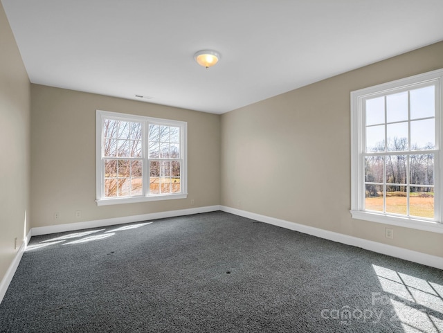 spare room featuring baseboards, dark carpet, and a wealth of natural light