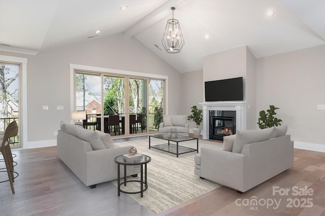 living room featuring baseboards, a glass covered fireplace, beamed ceiling, wood finished floors, and a notable chandelier