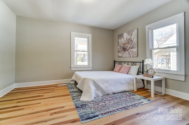 bedroom with multiple windows, baseboards, and wood finished floors