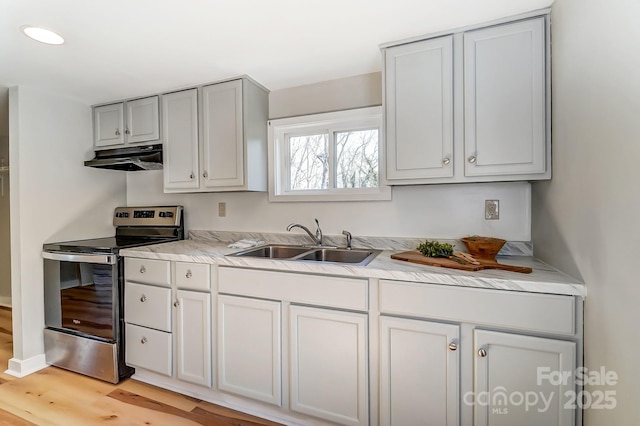 kitchen featuring light wood-type flooring, under cabinet range hood, a sink, light countertops, and stainless steel electric range oven