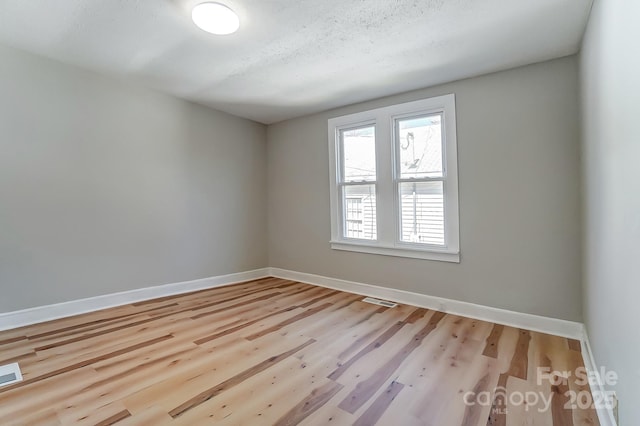 unfurnished room with wood finished floors, baseboards, and visible vents