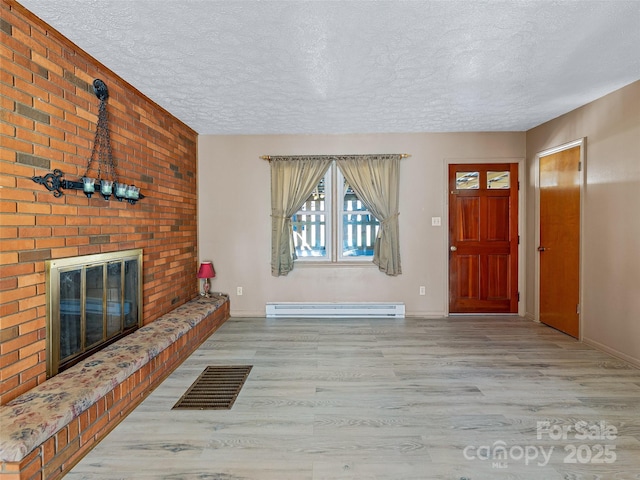 foyer entrance with light wood-style floors, a baseboard radiator, a brick fireplace, and visible vents