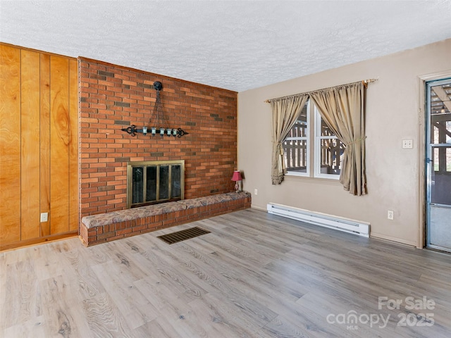 unfurnished living room with visible vents, a baseboard heating unit, a brick fireplace, a textured ceiling, and wood finished floors