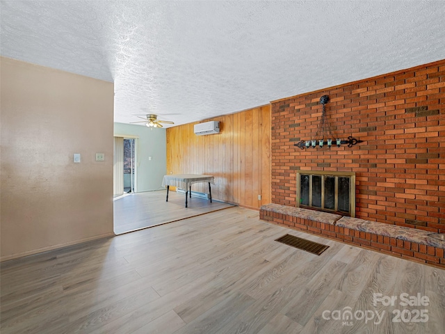 unfurnished living room featuring visible vents, a wall unit AC, a textured ceiling, light wood-type flooring, and a fireplace