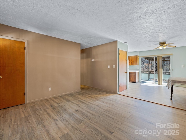 empty room with ceiling fan, a textured ceiling, light wood-type flooring, and baseboards