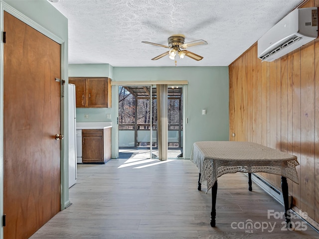 dining space featuring wooden walls, ceiling fan, a textured ceiling, light wood-style floors, and a wall mounted AC