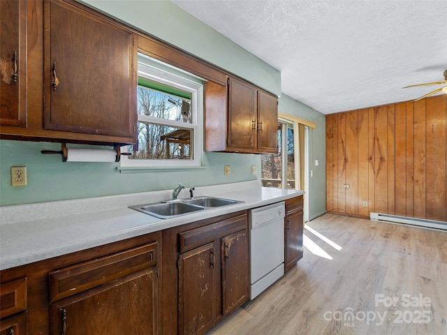 kitchen featuring white dishwasher, a baseboard heating unit, a sink, light countertops, and light wood finished floors