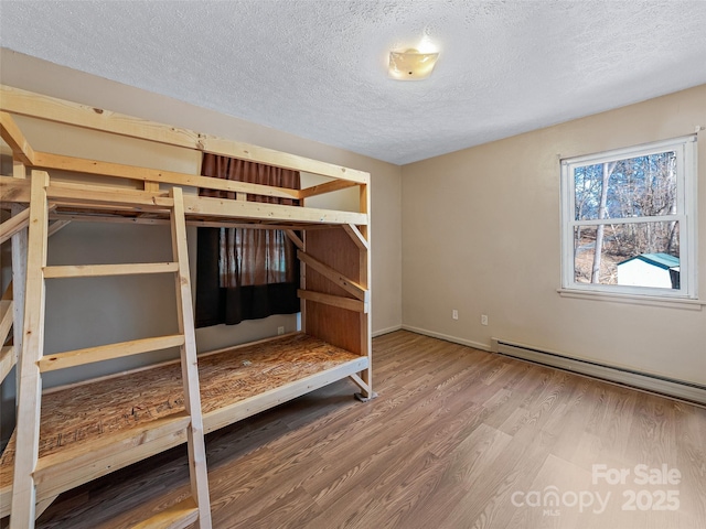 unfurnished bedroom featuring a textured ceiling, a baseboard heating unit, and wood finished floors