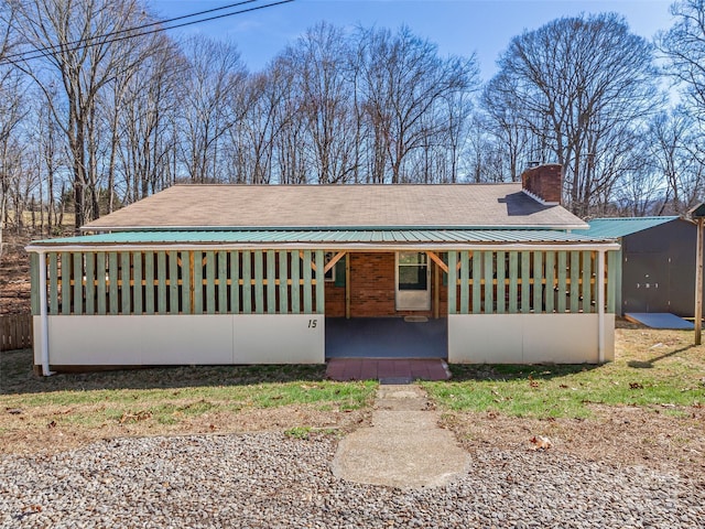 view of front of property featuring brick siding, metal roof, and a chimney