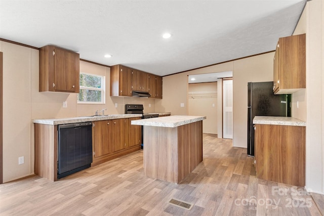 kitchen with brown cabinetry, a kitchen island, under cabinet range hood, light countertops, and black appliances