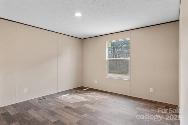 empty room featuring ornamental molding, visible vents, a textured ceiling, and wood finished floors